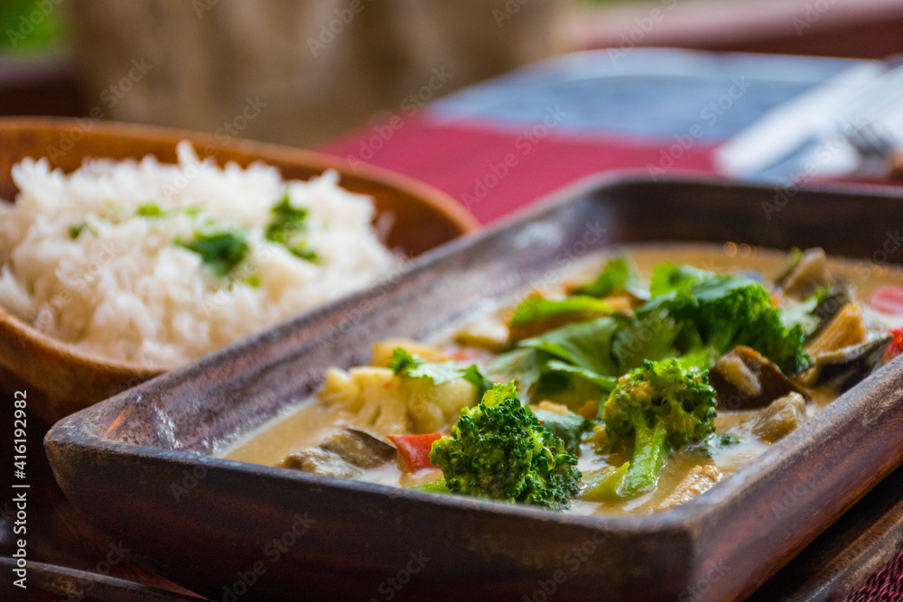 vegan cuisine with drinks on a table set for two. These healthy options are Thai Green Curry with white rice and Pad Thai. Glasses of white wine and beer are also on the candlelit table vegan cuisine with drinks on a table set for two. These healthy options are Thai Green Curry with white rice and Pad Thai. Glasses of white wine and beer are also on the candlelit table
