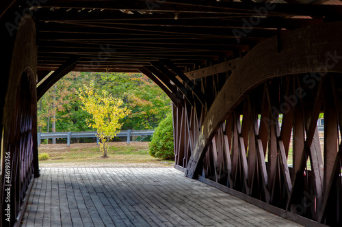 looking through wooden, covered bridge to a yellow tree