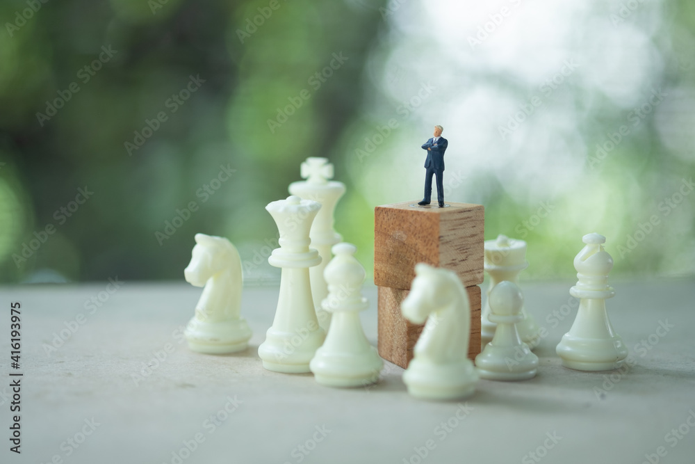 Miniature businessman standing on wooden block above white chess. Strategic concept