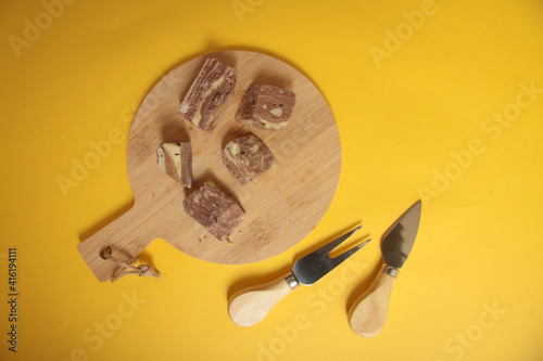 pieces of sherbet on wooden cutting board, knife and a fork on yellow background flat lay. Turkish delifght concept