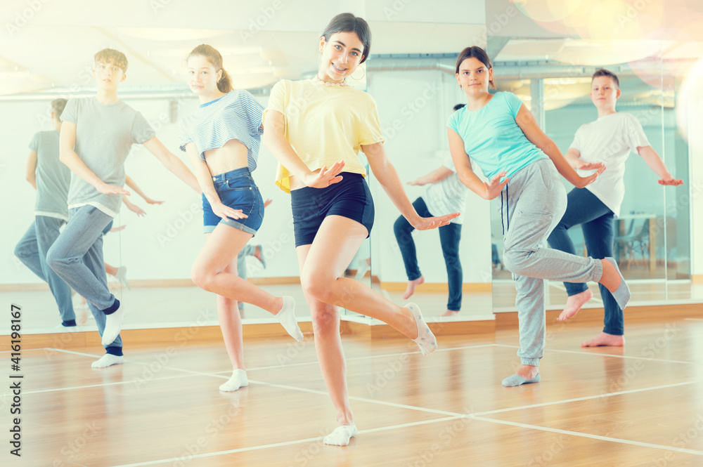 Diligent friendly smiling teenagers learn dance movements in dance class