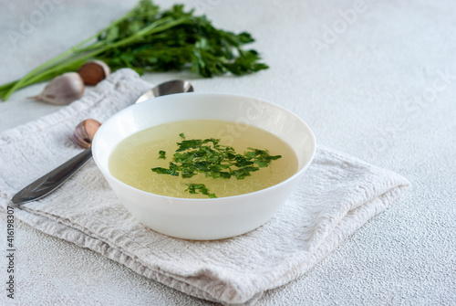 Chicken broth with parsley in bowl on white table