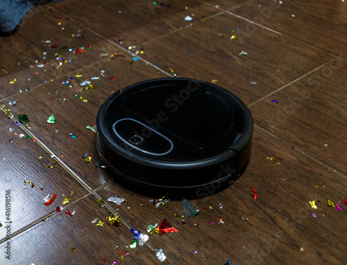 Modern black robotic vacuum cleaner removing litter from brown wooden floor. Cleaning at home, top view. 