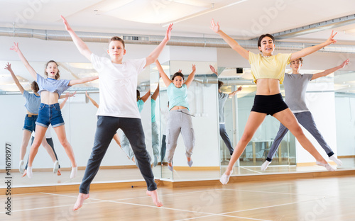 Satisfied teenage boys and girls jumping having fun during dance class