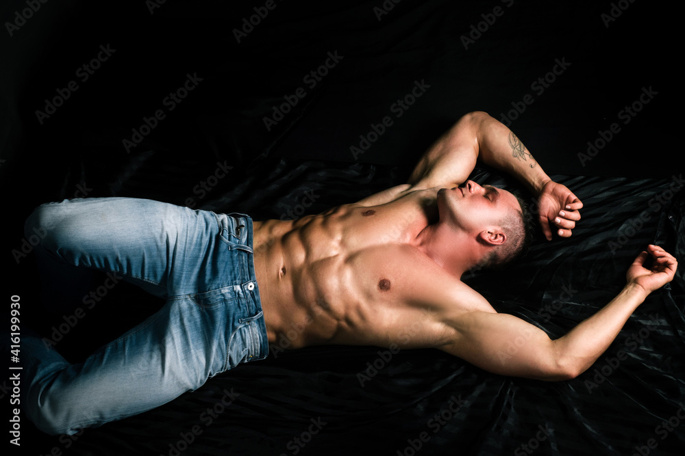 Muscular male torso, bare abs. Man lying on bed. Sexy guy in bedroom.