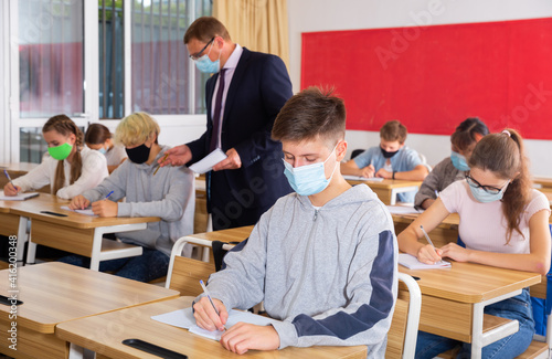 Portrait of diligent schoolboy wearing protective face mask sitting in class working with classmates, new normal education during pandemic