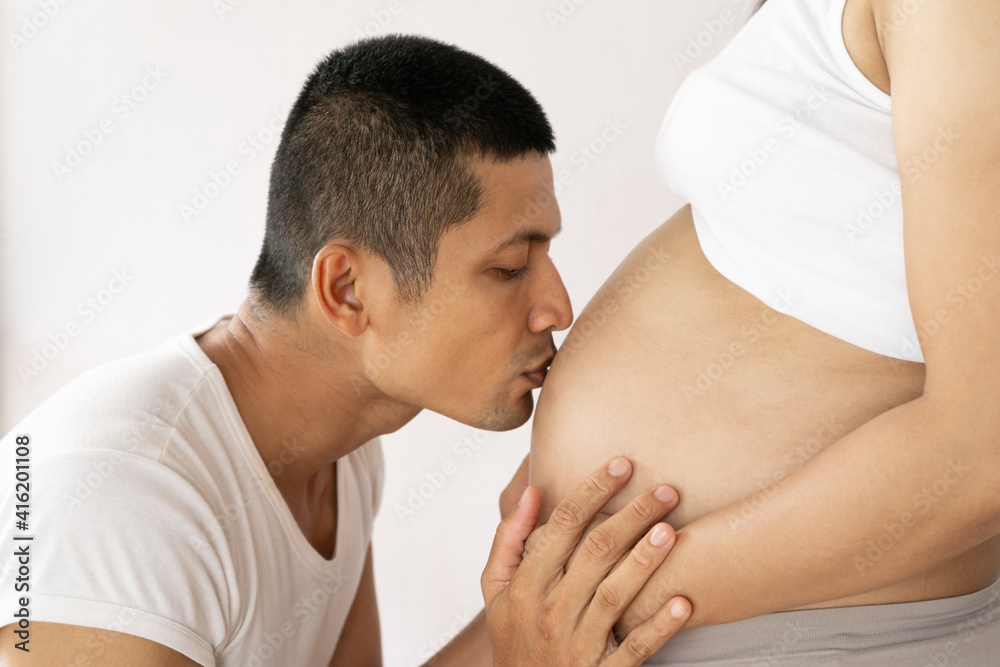 Portrait husband is kissing to pregnant womans baby moving inside . Portrait husband is kissing to pregnant womans baby moving inside .