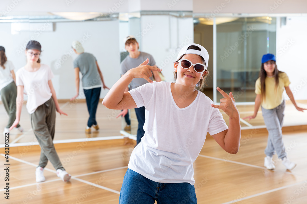 Teenage girl hip hop dancer in casual clothes, cap and sunglasses exercising with friends at dance center
