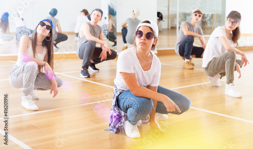 Positive teen girls and boys hip hop dancers squatting during group dance workout