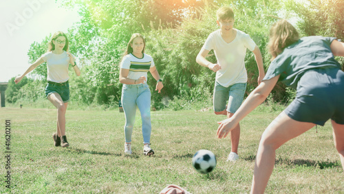 Cheerful teen friends gaily spending time together on summer day, playing with ball outdoors
