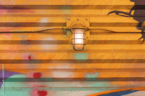 Colorful abstract wall, vivid colors on metal. Exterior urban drawing. Hanging lamp bulb lighting. Orange, yellow vivid close up