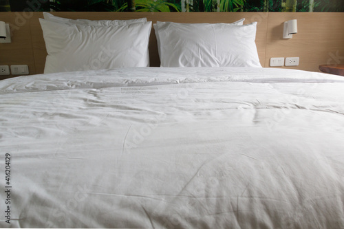 White pillows, duvet and duvet case on a wooden bed. White bed linen. Bedroom with bed and bedding. Front view.