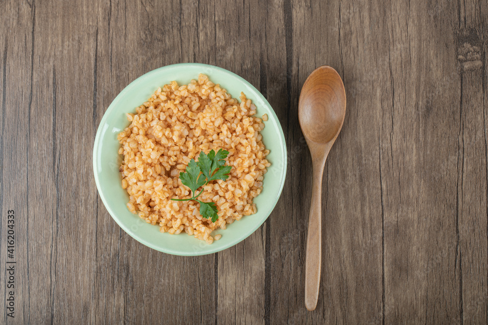 Delicious bulgur with greens on a green plate with spoon Delicious bulgur with greens on a green plate with spoon