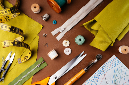 Flat lay composition of sewing accessories, scissors, patterns, fabrics on a brown background, top view. The desktop of a fashion designer, tailor in an atelier. Vintage style sewing concept photo