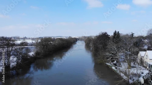 River in France with snow beautiful french snowy countryside. aerial drone view of trees covered by the snow in border frozen river by sunny day with clouds and blue sky