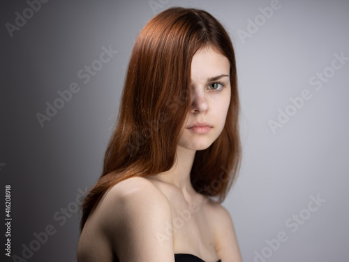 Beautiful woman with loose red hair on a gray background bared shoulders portrait