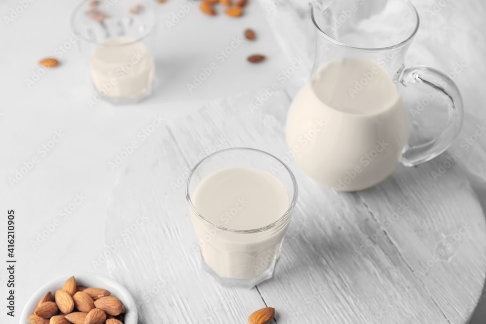 Jug and glass of tasty almond milk on light background