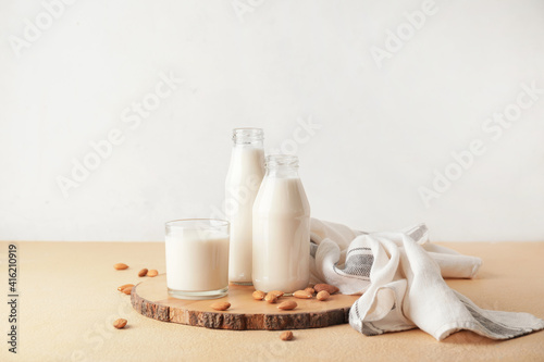 Bottles and glass of tasty almond milk on color table