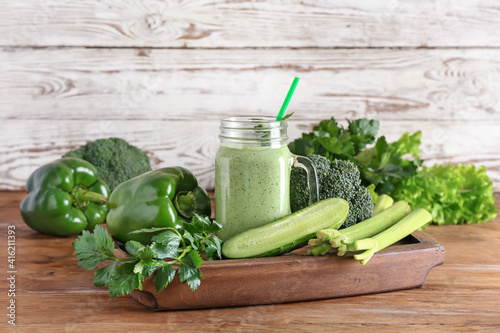 Mason jar of healthy smoothie with green vegetables on wooden background