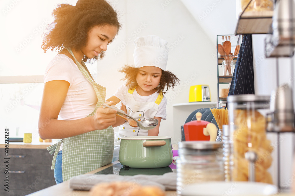 Cute African-American sisters cooking in kitchen Cute African-American sisters cooking in kitchen
