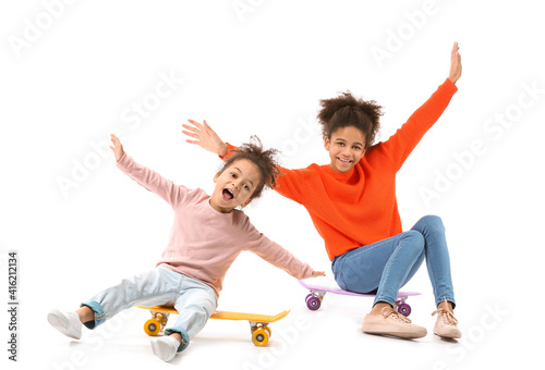 Portrait of cute African-American sisters with skateboards on white background
