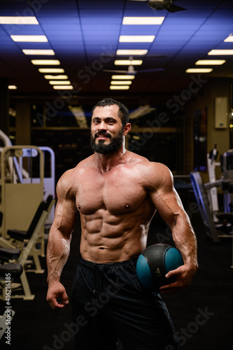 happy smiling strong young bearded athlete with medicine heavy ball in blue lit night sport gym