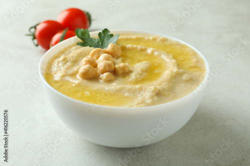 Bowl of hummus and tomatoes on white textured background
