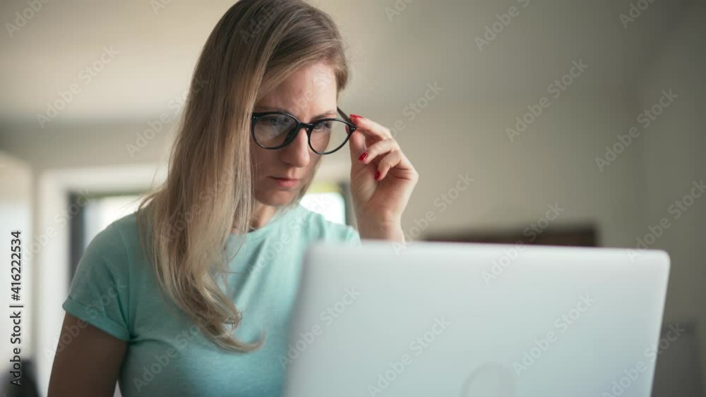 Young adult woman in glasses working on a laptop from home. Remote employee concept. Young adult woman in glasses working on a laptop from home. Remote employee concept.