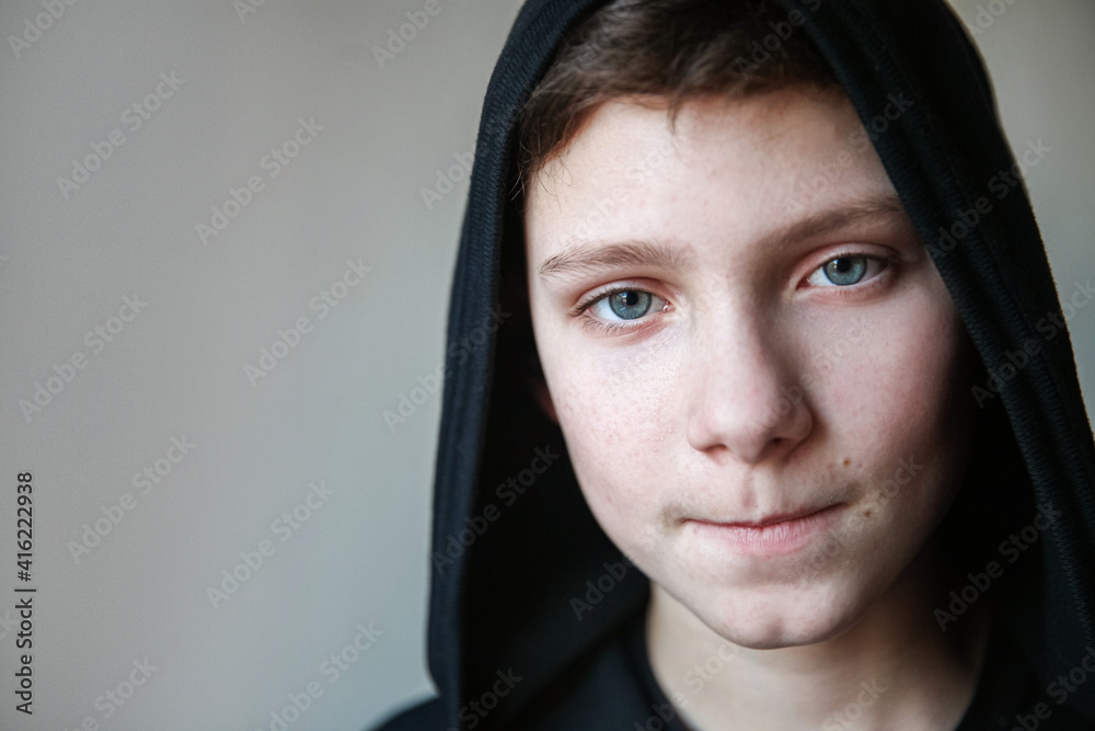 Portrait of a teenage boy with blue eyes and pursed lips. The boy in the black hood