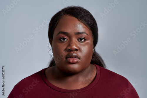Close up portrait of serious plus size young african american woman in casual clothes looking at camera while posing isolated over gray background