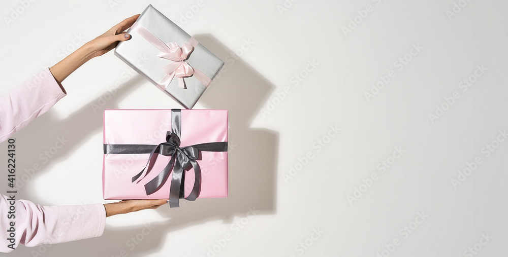 Obraz premium Womens day celebration. Female hands holding two wrapped gift boxes against light background with shadow. panoramic banner with copy space for text