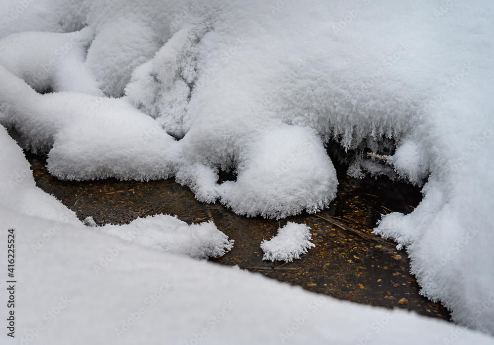 Freezing stream in the forest, close-up. textured snow grainy surface on the banks of the stream, you can see the bottom with small stones and clear water. Natural source of water