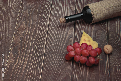 Wine bottle, grapes and cheese lie on the background of wooden boards