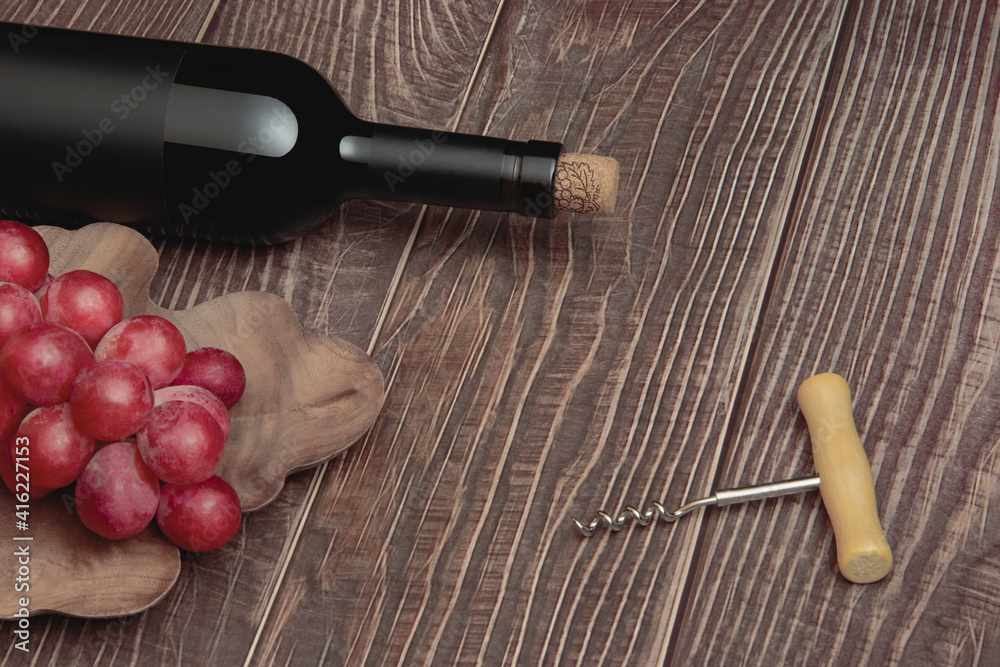 Expensive wine bottle with corkscrew and grapes on conceptual wooden boards background