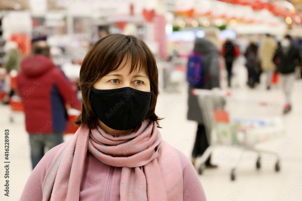 Woman in black protective mask in a shopping mall on people background. Customers in store during quarantine at covid-19 pandemic	