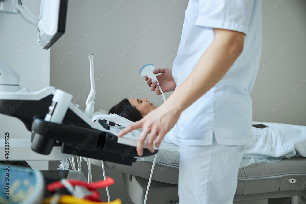 Physician with a transducer standing before an ultrasonography apparatus console Physician with a transducer standing before an ultrasonography apparatus console
