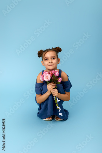 cute happy little girl holding bouquet of pink roses on blue background.
