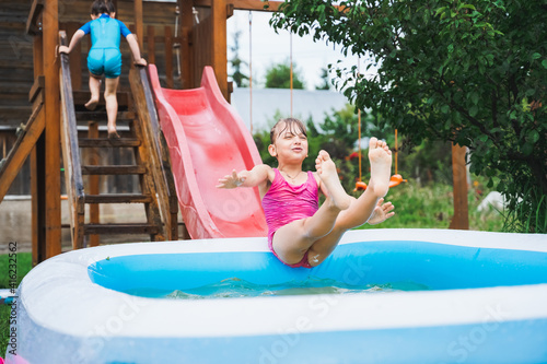 Staycation at home. Little girl in swimsuit rolls down slide into inflatable rubber pool. Swim activity in backyard of country house. Summer,relaxation on isolation,quarantine of coronavirus covid-19 photo