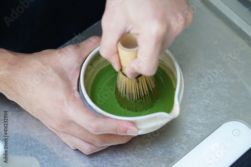 Barista Using bamboo whisk (chasen) stir matcha and hot water in the bowl on table, Mixing green tea in bowl.