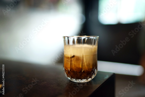 Iced black coffee with milk - A glass of cold brew coffee topped with milk foam on blurred background.