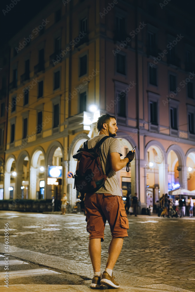 Tourist man with backpack walk on the night summer street in Italy. Vertical photo. Bologna