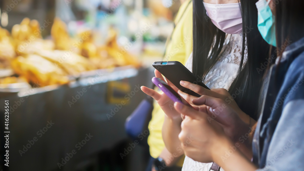 Asian women holding smartphones in a food market.
