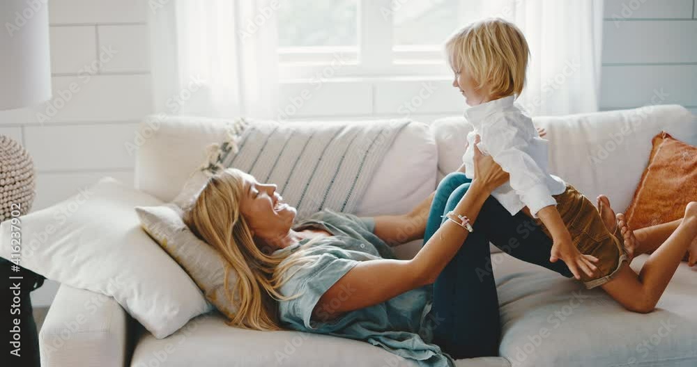 Mother and cute son spend quality time together at home, playing on the couch, pretending to fly, laughing and smiling, quality family time