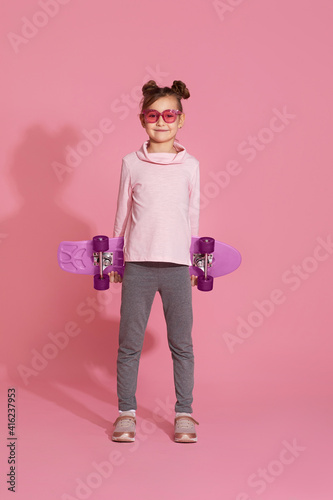 adorable little child girl with skateboard over pink background.
