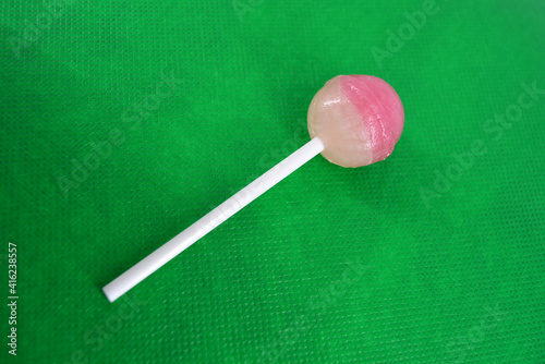Delicious round sweet candy, white pink lollipop on white plastic wand located on green fabric background. 