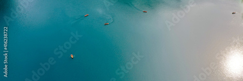 Boats from the air. Aerial view of a lake in Italy. Summer landscape with clear water on a sunny day. Top view of the boat from a drone. The clouds are reflected in the water © VIK