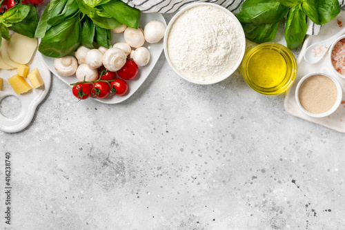 Pizza ingredients on a culinary background. Flour, yeast, salt, water, olive oil, parmesan, cheese, mozzarella, basil, tomatoes on the table. The concept of preparing for baking pizza or pie. Top view