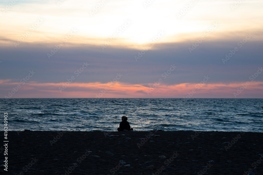 Orange sunset on the sea, the silhouette of a man on the background of the sunset. A girl sits on the beach at sunset.