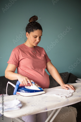 Pregnant woman at home ironing baby laundry.