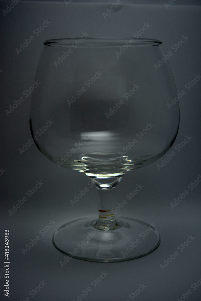A beautiful and unusual glass glass, a glass for cognac, spirits is located on a white background with an interesting light shade. A beautiful and unusual glass glass, a glass for cognac, spirits is located on a white background with an interesting light shade.
